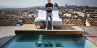Charlie MacGregor, chief executive officer and founder of The Student Hotel (TSH) at the opening of his first Italian hybrid hotel, TSH Florence Lavagnini. Charlie is pictured standing in front of a bed on a platform above the rooftop pool in front of the Duomo in the Tuscan capital, Florence.