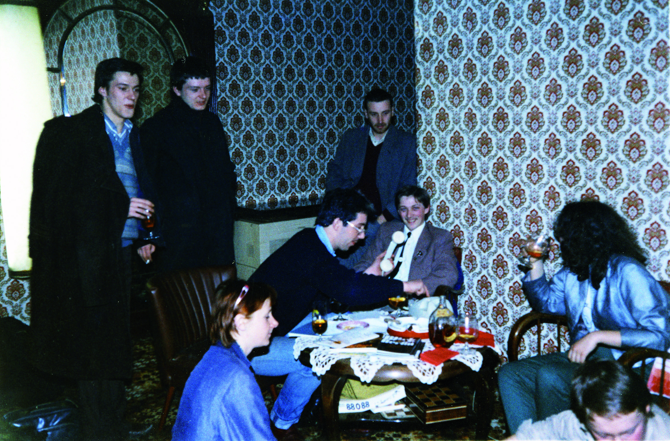 Mark Reeder (seduto di fianco davanti alla parete) con i Joy Division (in piedi, da sinistra, Bernard Sumner e Ian Curtis) - dall'archivio privato di Mark Reeder